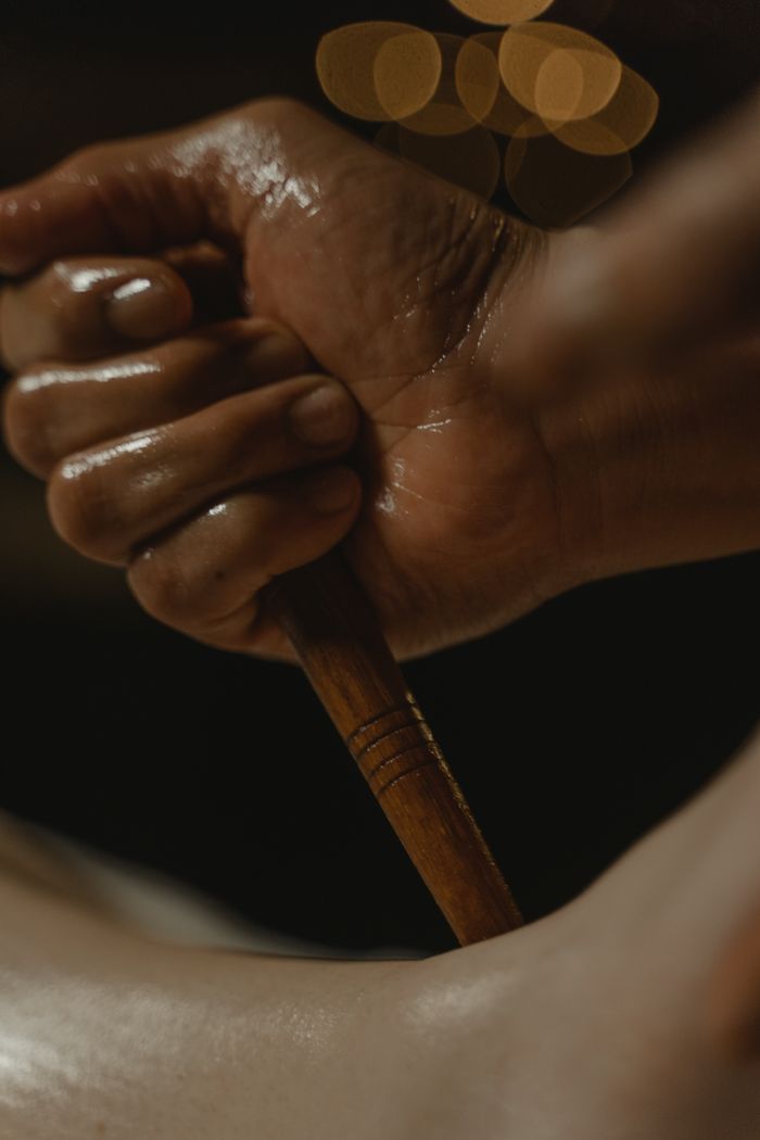about-01 A close-up of a hand holding a wooden massage tool, set against a dark background.